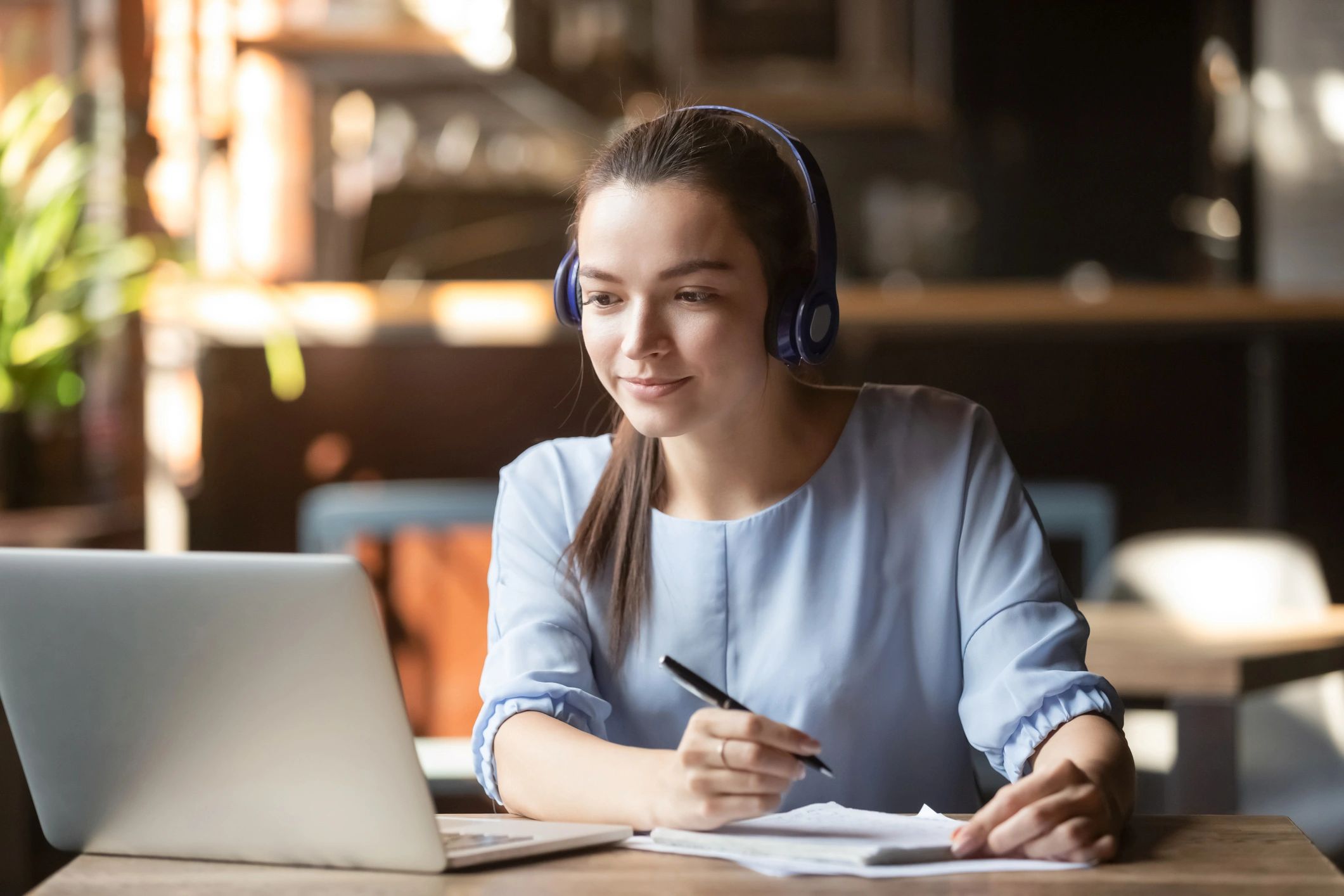 A woman wearing headphones is writing on paper.