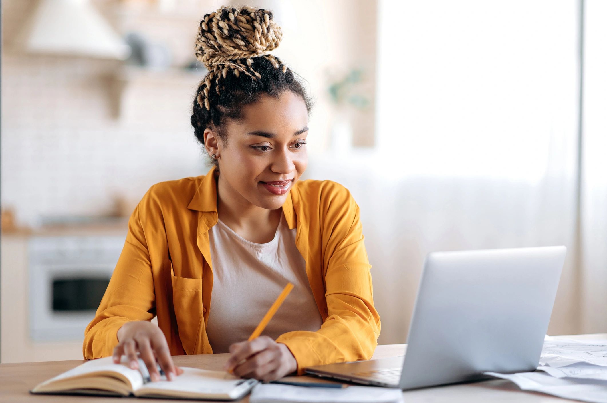 A woman sitting at a table with a laptop and writing.