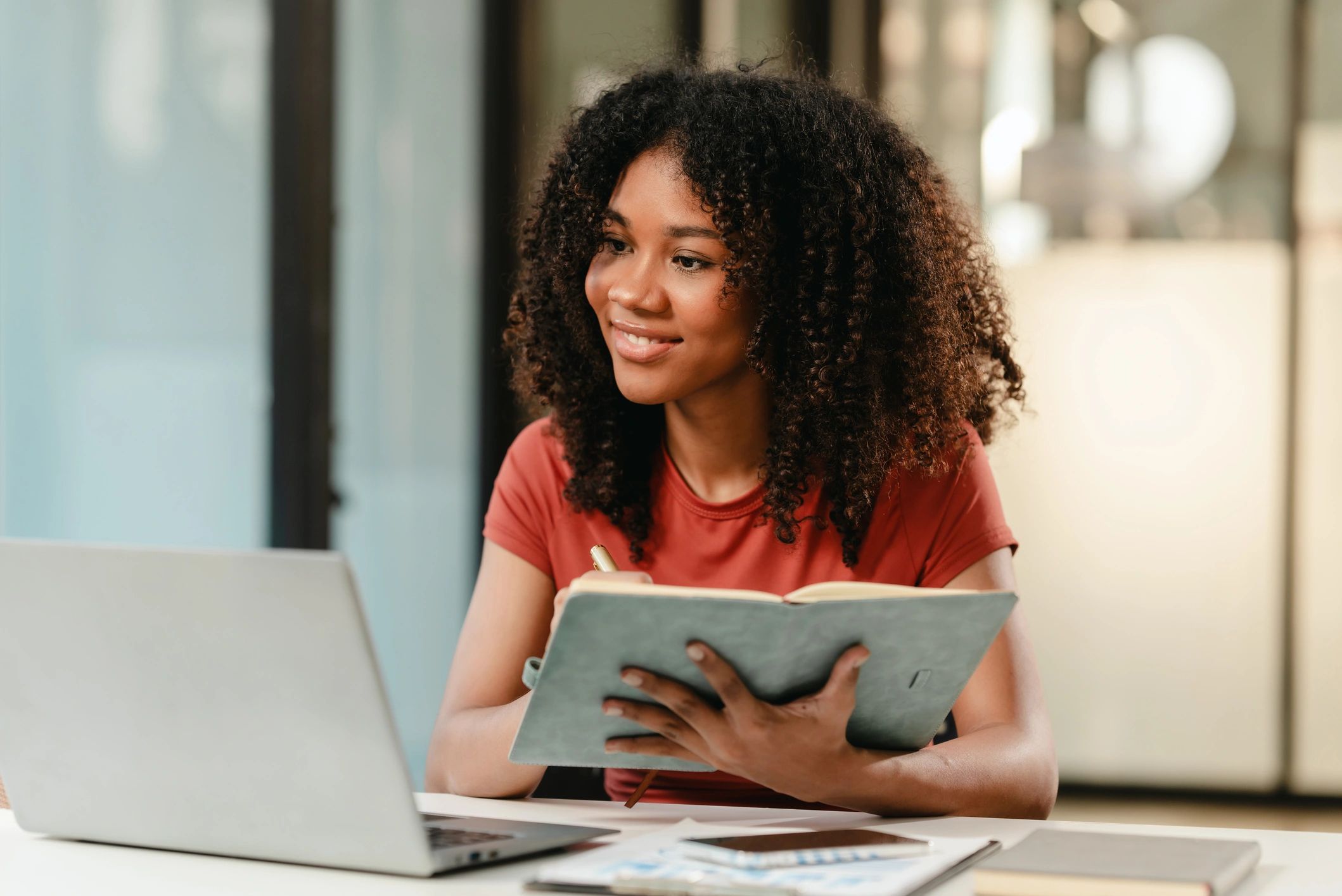 A woman sitting at a table with a laptop and book.